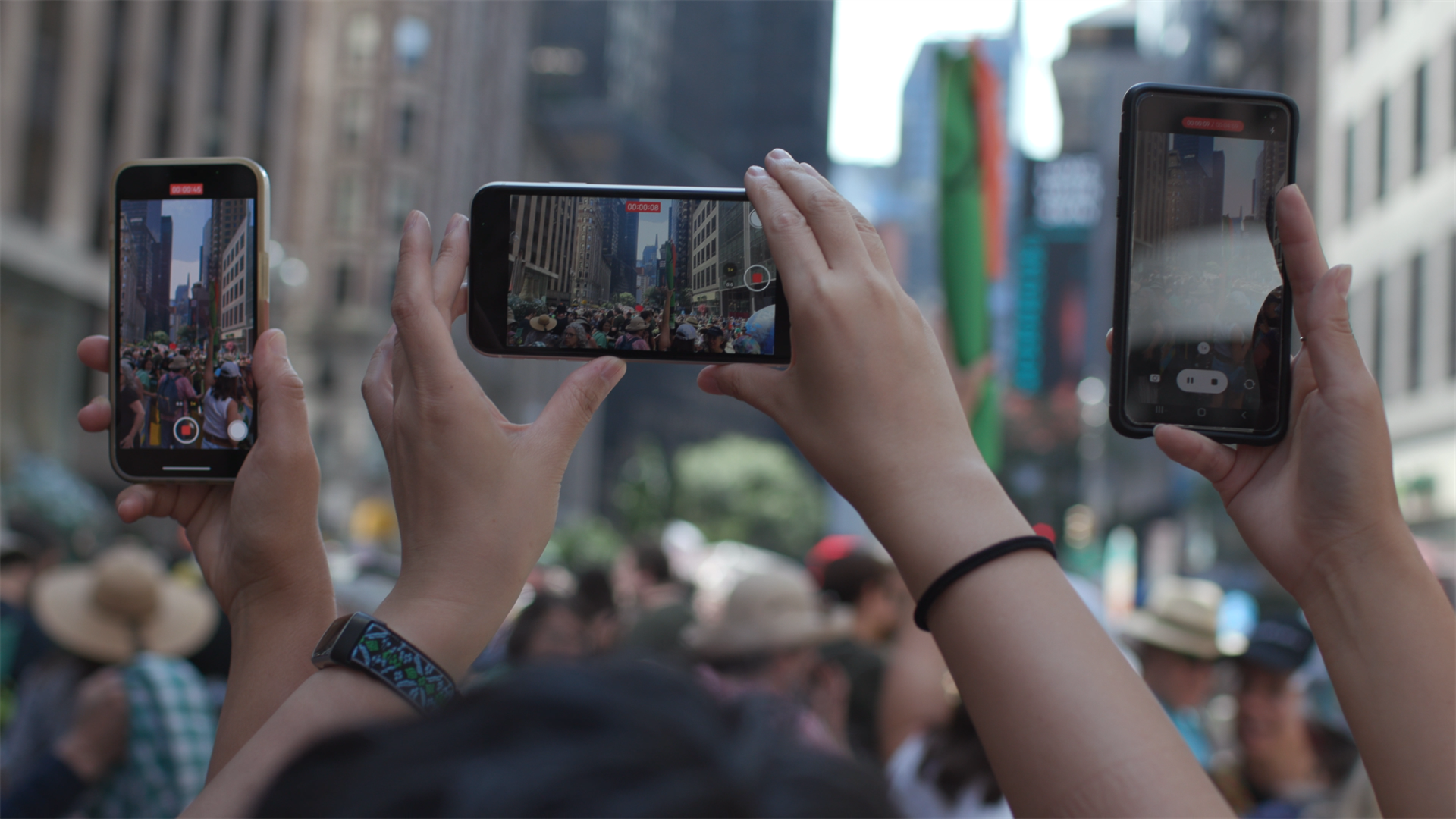 Hands of individuals holding smartphones, capturing a climate protest.